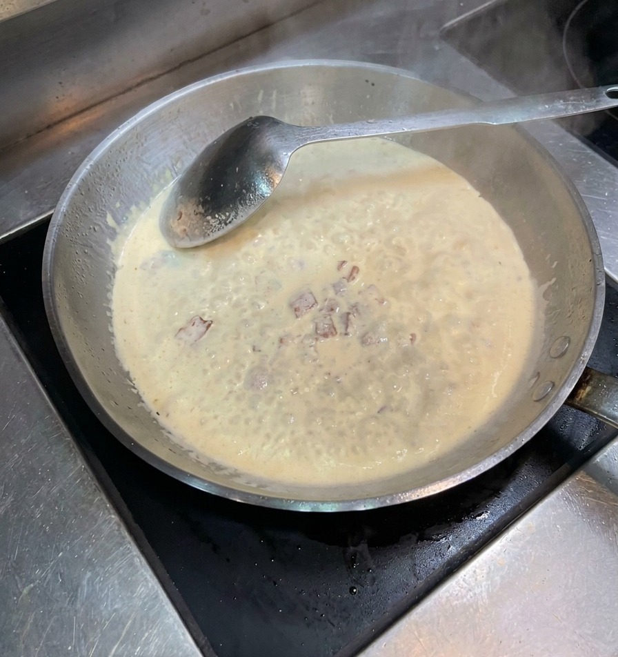 Poivre noir et sel saupoudrés dans une poêle de crème et lardons frémissants.