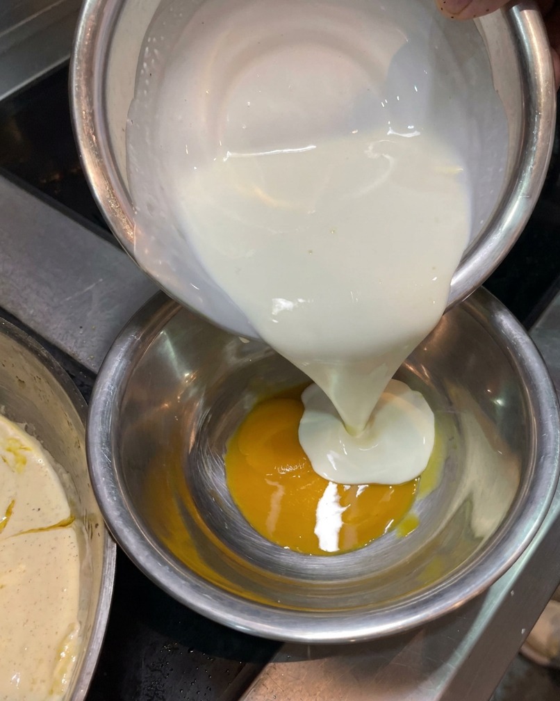 Crème entière versée depuis un bol argenté dans un autre bol contenant un jaune dœuf éclatant.
