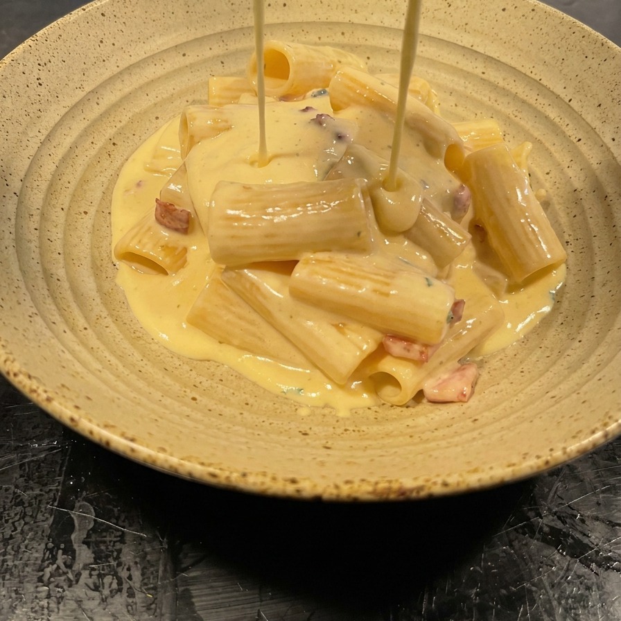 Sauce veloutée versée depuis la poêle sur un dôme de rigatoni dans un bol moucheté.