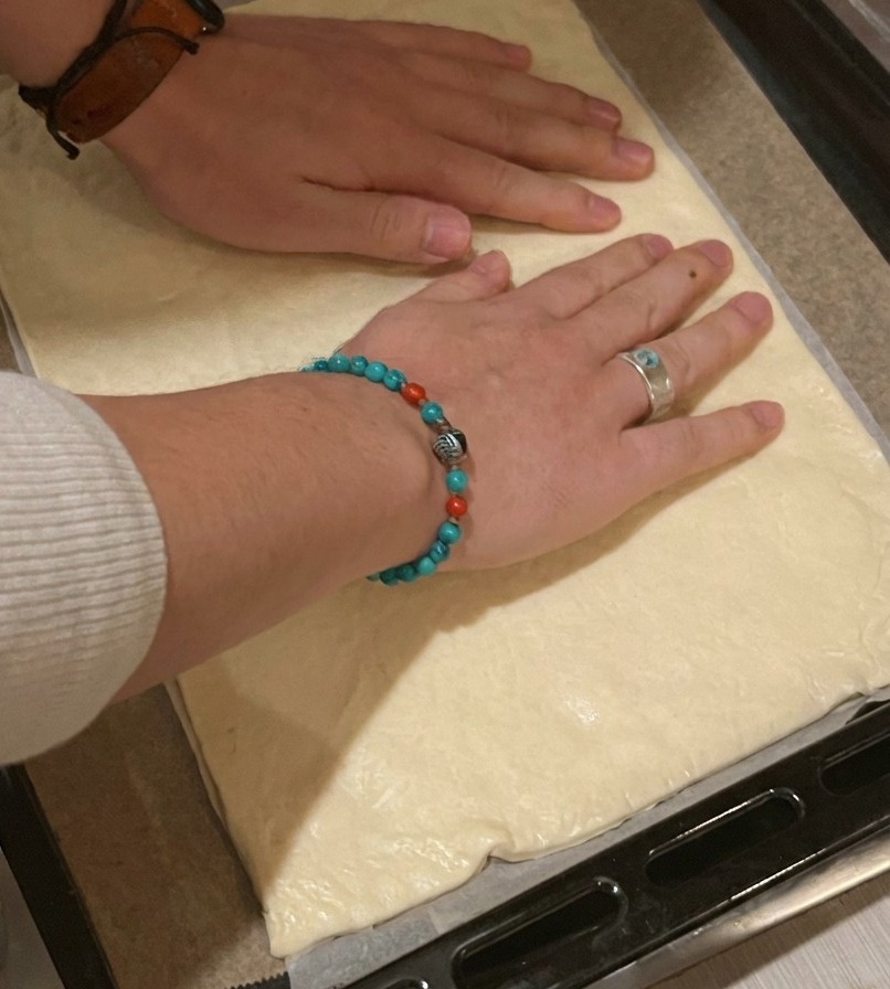 Une personne déposant une pâte à pizza rectangulaire sur une plaque de cuisson recouverte de papier sulfurisé.