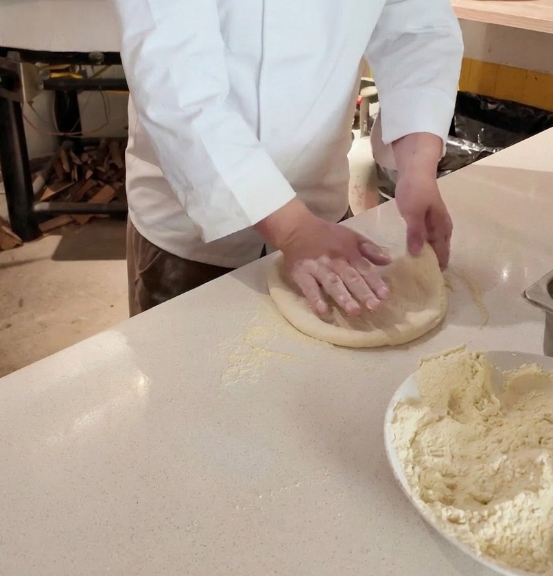 Mains dun chef étirant un pâton de pizza sur un plan fariné devant un four à bois.