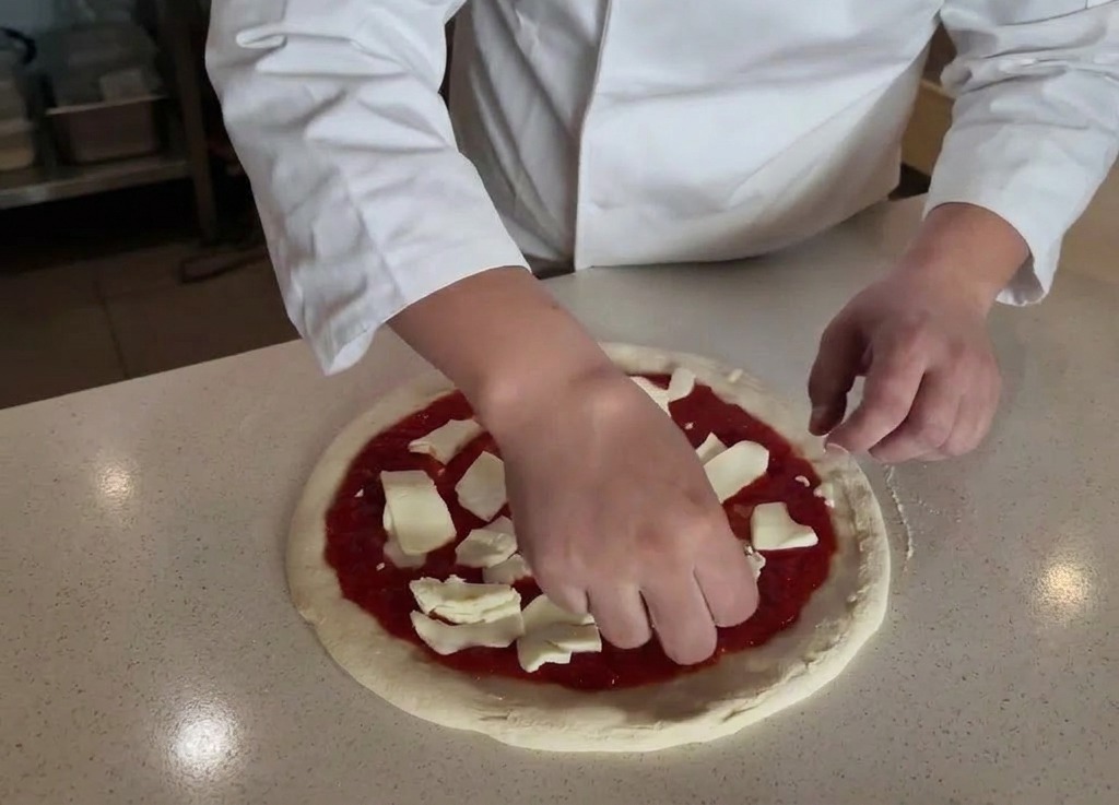 Mains dun chef déposant des morceaux de mozzarella fraîche sur une base de pizza à la tomate.
