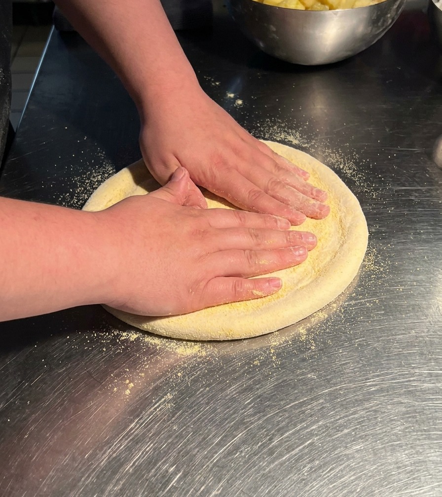 Les mains dune personne pressant un morceau circulaire de pâte sur une table en inox pour létirer en un large disque.