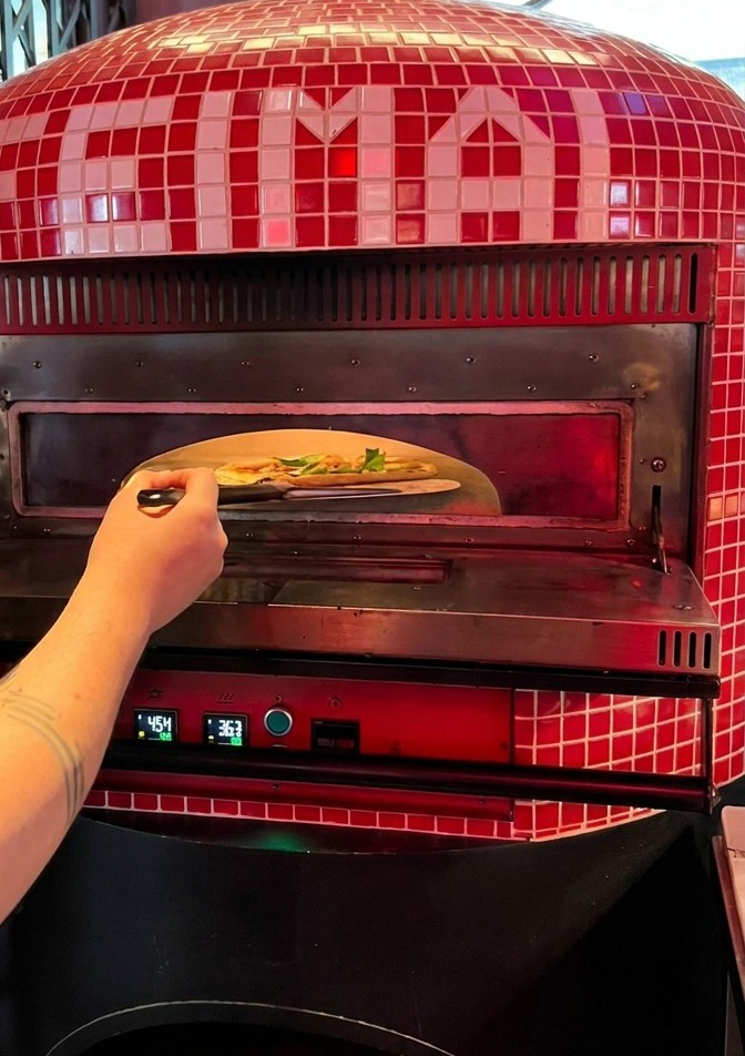 Une personne faisant glisser une pizza crue depuis une pelle en métal dans la bouche incandescente dun four à pizza traditionnel rouge.