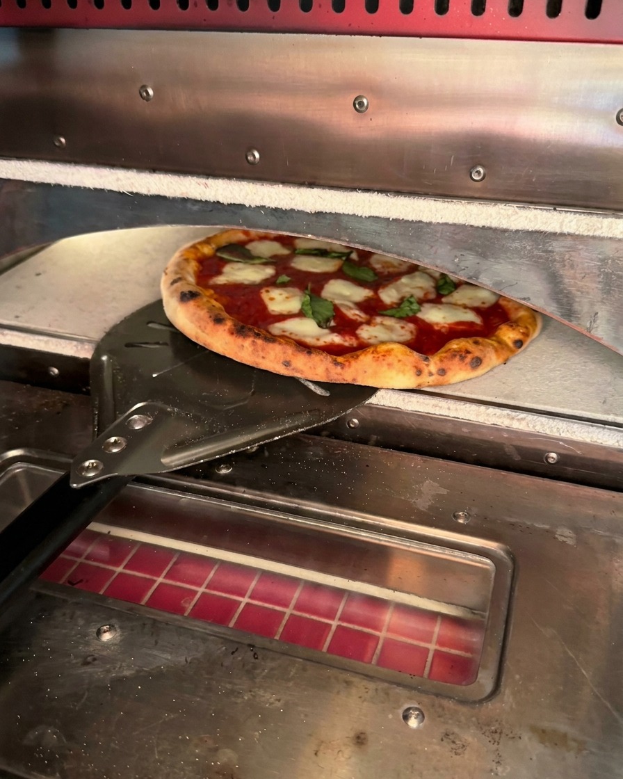 Une pizza fraîchement cuite aux bords mouchetés de brun retirée du four à laide dune pelle en métal.