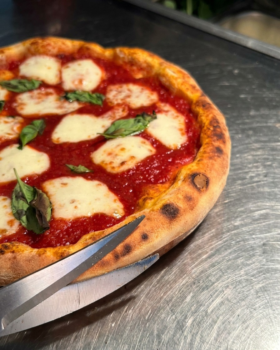 Gros plan de ciseaux de cuisine en métal coupant la croûte gonflée dune pizza Margherita brûlante.