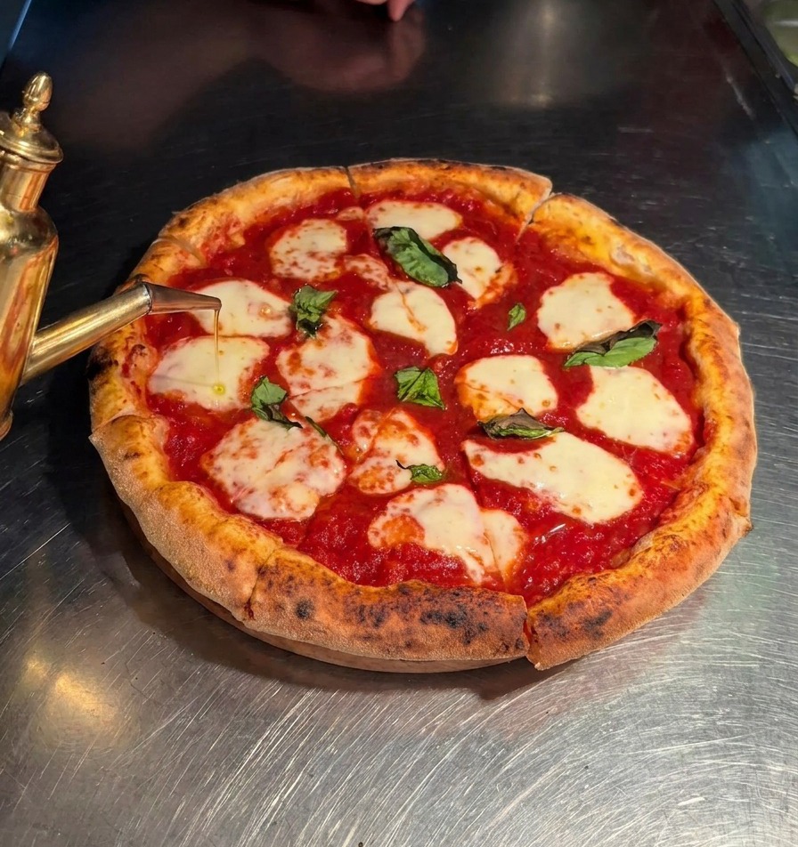 De lhuile dolive extra vierge versée dun huilier à bec doré sur une pizza Margherita tranchée.