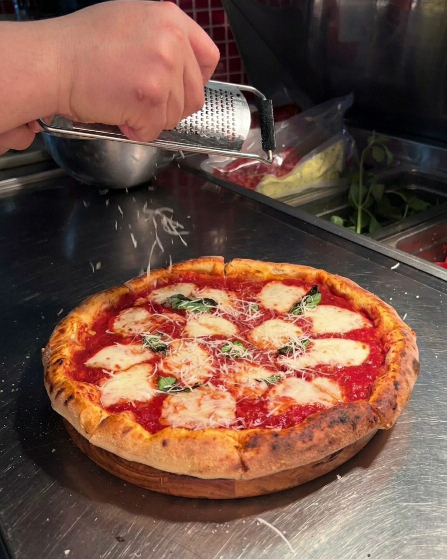 Gros plan dune main utilisant une râpe microplane pour râper du parmesan frais sur une pizza napolitaine.