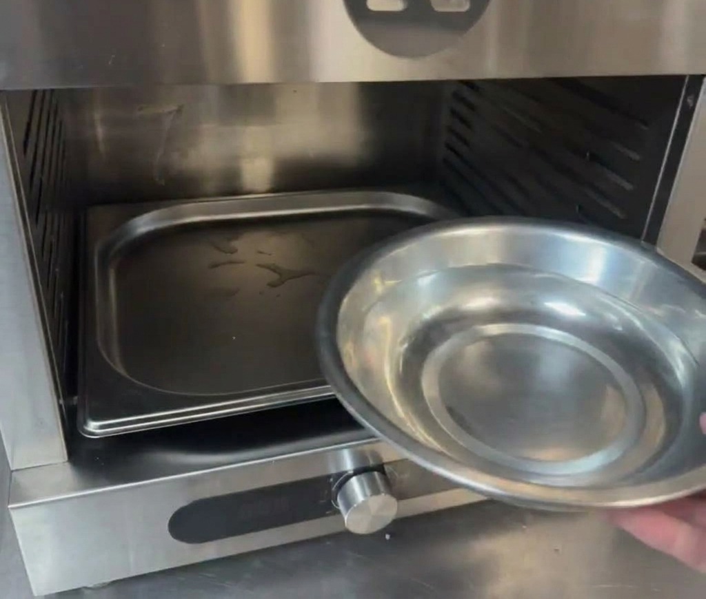 Une main versant de leau dun petit bol en métal dans un plateau situé au fond de la chambre dun four professionnel.