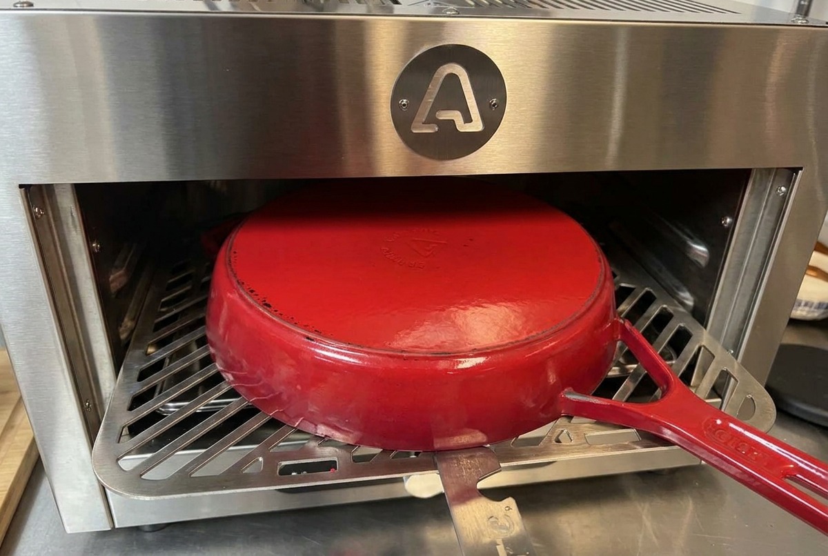 Une cocotte en fonte émaillée rouge posée à lenvers sur une grille métallique à lintérieur dun four en inox.