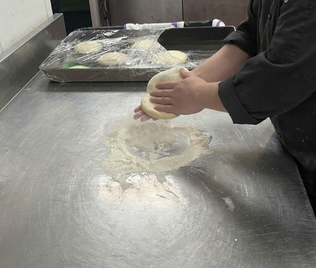 Des mains étirant une pâte à pizza pâle sur une surface farinée pour former un cercle plus grand.