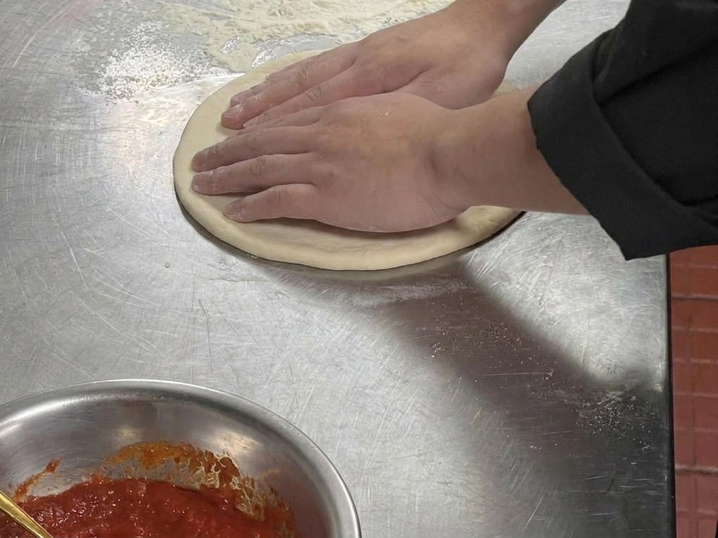 Gros plan de mains pressant le bord dun cercle de pâte aplati pour créer un contour surélevé.