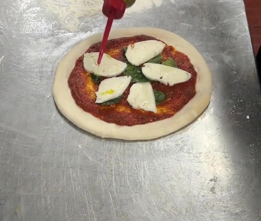 Une bouteille souple rouge versant de lhuile dolive extra vierge sur une pizza garnie de sauce tomate, basilic et mozzarella.