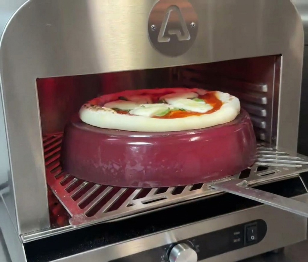 Une pizza cuisant sur une cocotte en fonte rouge à lintérieur dun four, la croûte commençant à lever et à dorer.
