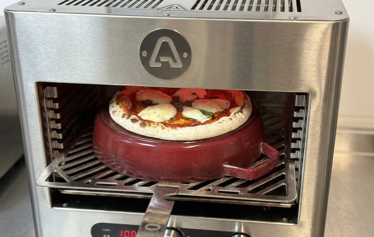 Une pelle à pizza métallique insérée dans le four pour faire pivoter une pizza presque cuite sur une cocotte en fonte.