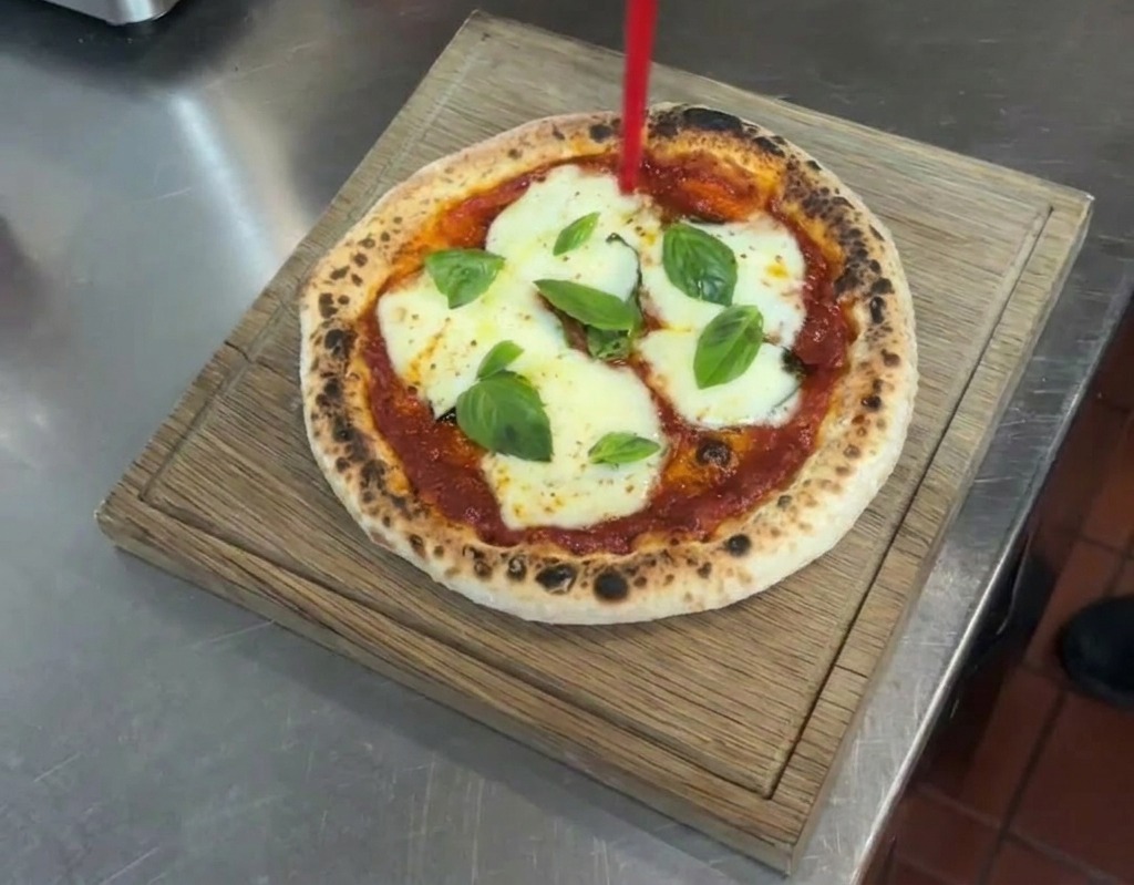 Un filet dhuile dolive extra vierge versé dune bouteille sur une pizza Margherita terminée posée sur une planche en bois.