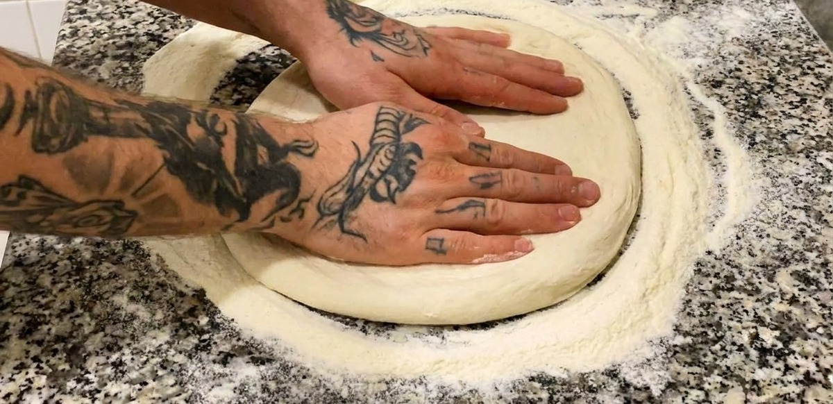 Deux mains pressant une base de pizza ronde et farinée sur un plan de travail en marbre gris.