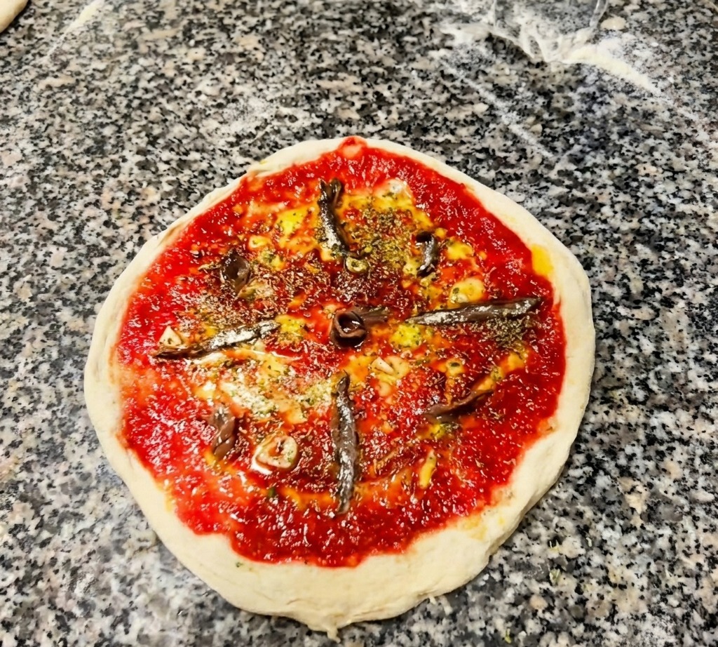 Vue de dessus dune pizza crue garnie de tomate, dherbes et de filets danchois disposés en rayons.