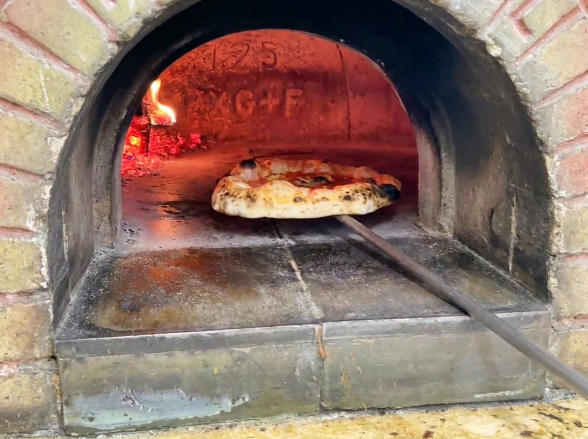 La pizza terminée sortant du four, montrant une croûte dorée avec des taches de brunissage caractéristiques.