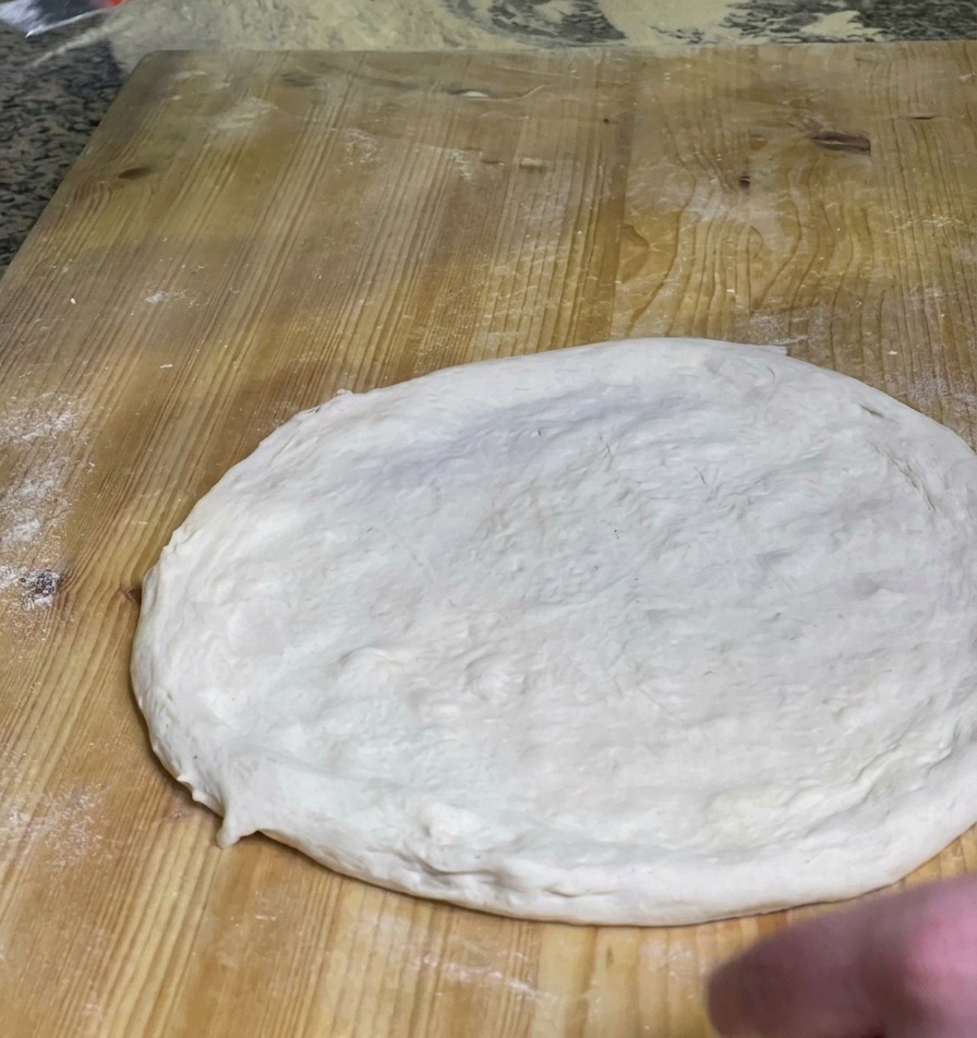 Un chef étalant une couche de sauce tomate rouge vif sur le centre dune pâte à pizza crue sur une planche en bois