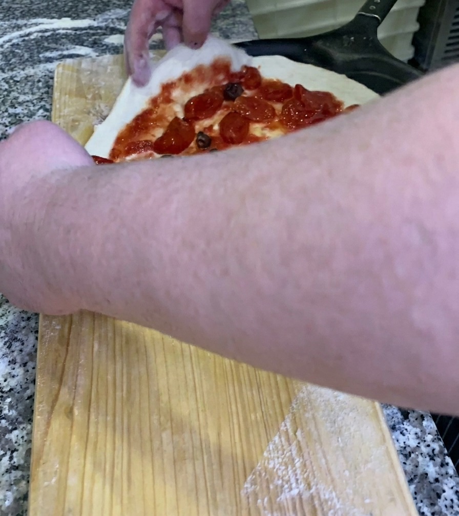 Le chef faisant glisser une pizza crue garnie sur une pelle à pizza en métal noir depuis un plan de travail en bois.