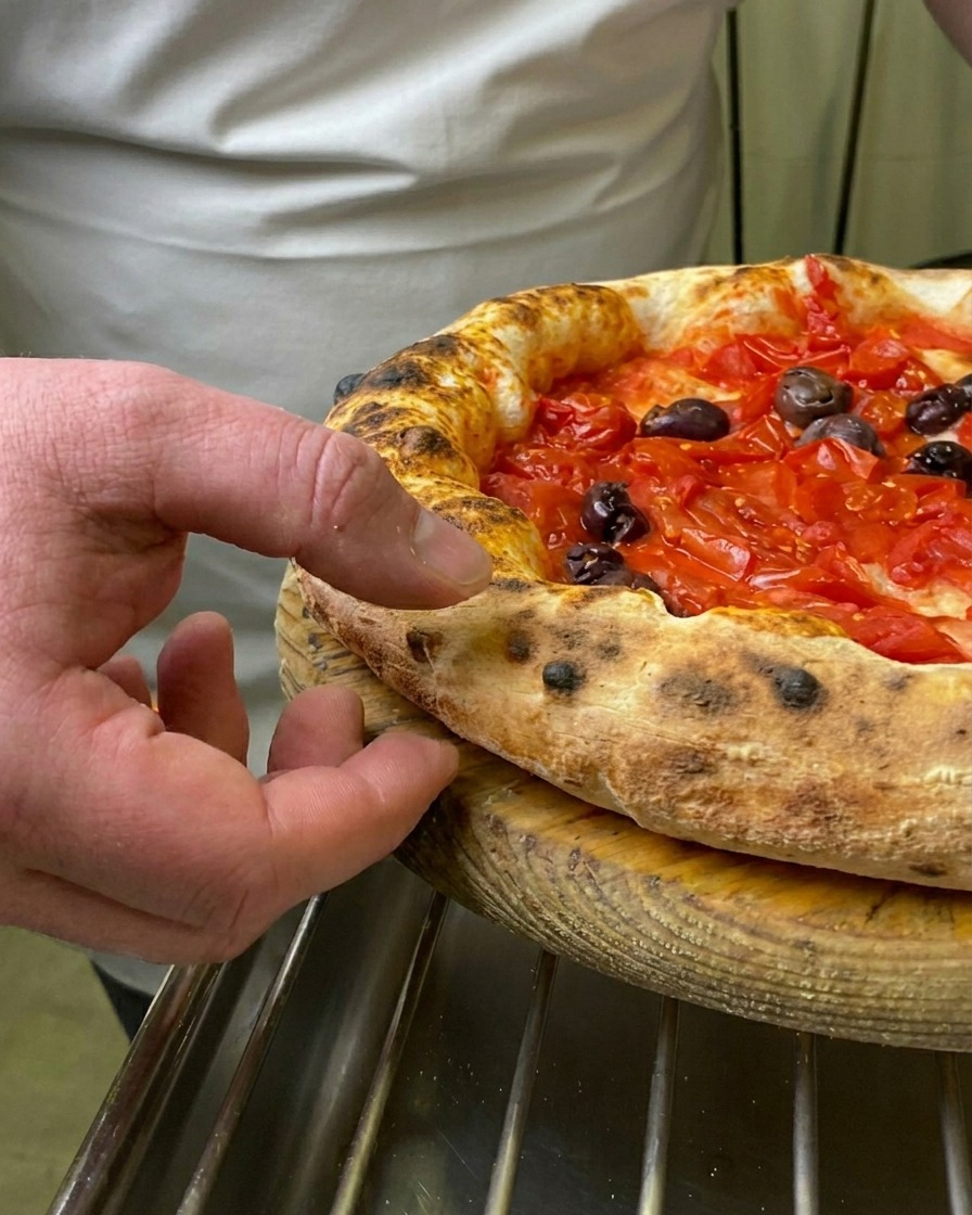 Le doigt dun chef pressant la croûte soufflée et grillée dune pizza Marinara fraîchement sortie du four.