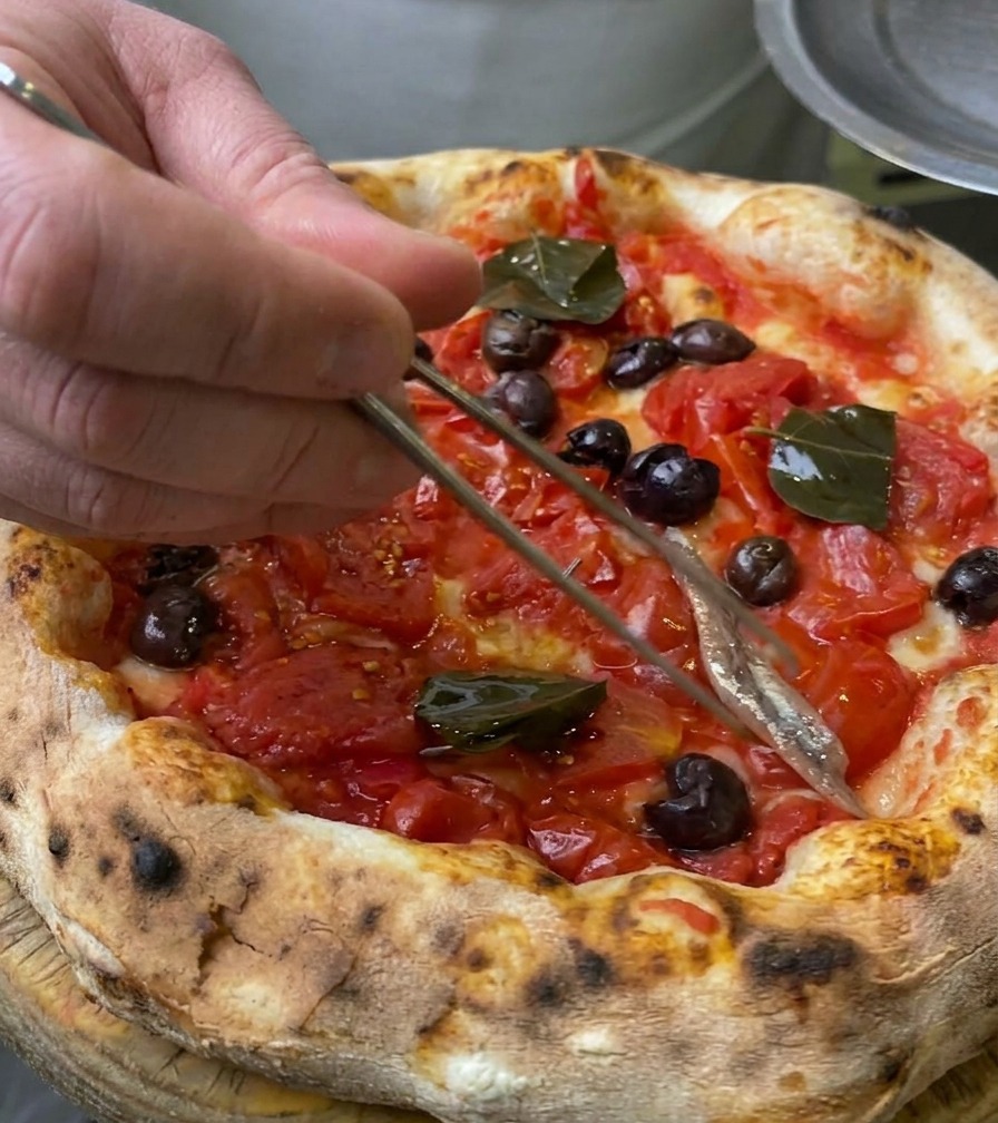 Gros plan dun filet danchois argenté déposé sur une croûte de pizza à laide dune pince culinaire en métal.