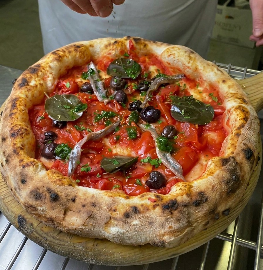 Une main parsemant du basilic frais sur le centre dune pizza Marinara cuite.