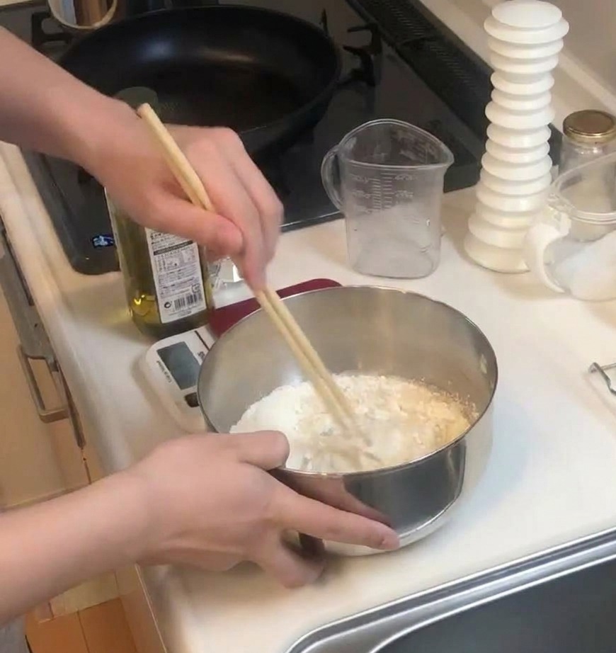 Une personne utilisant des baguettes en bois pour mélanger la farine et les liquides dans un bol en inox.