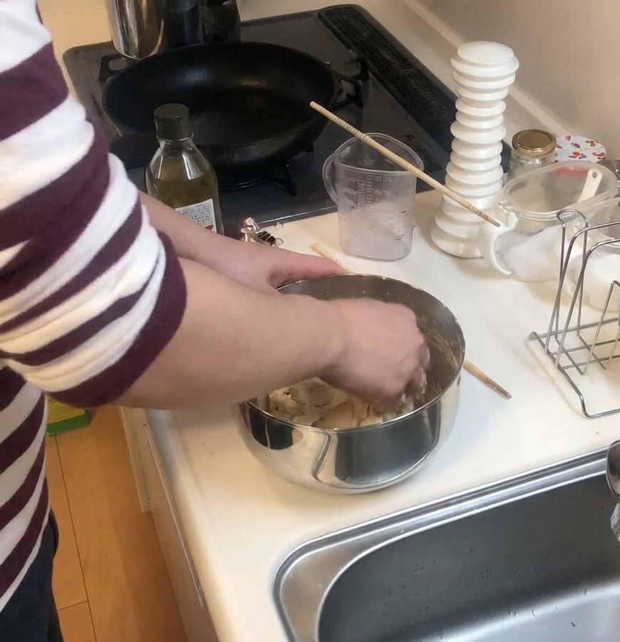 Des mains pétrissant la pâte à pizza dans un bol en inox, à côté dune bouteille dhuile dolive.