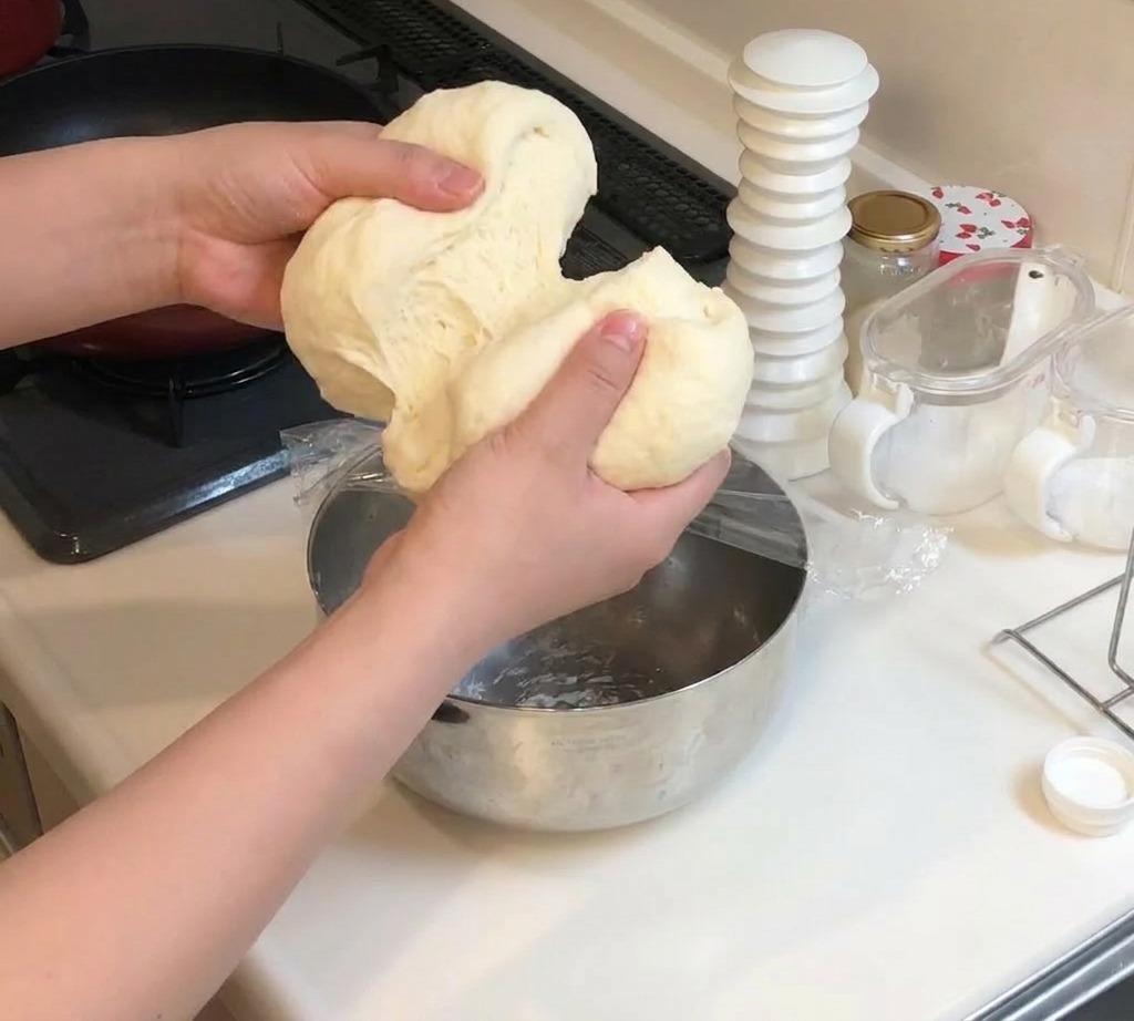 Deux mains séparant en deux une boule de pâte à pizza douce et élastique.