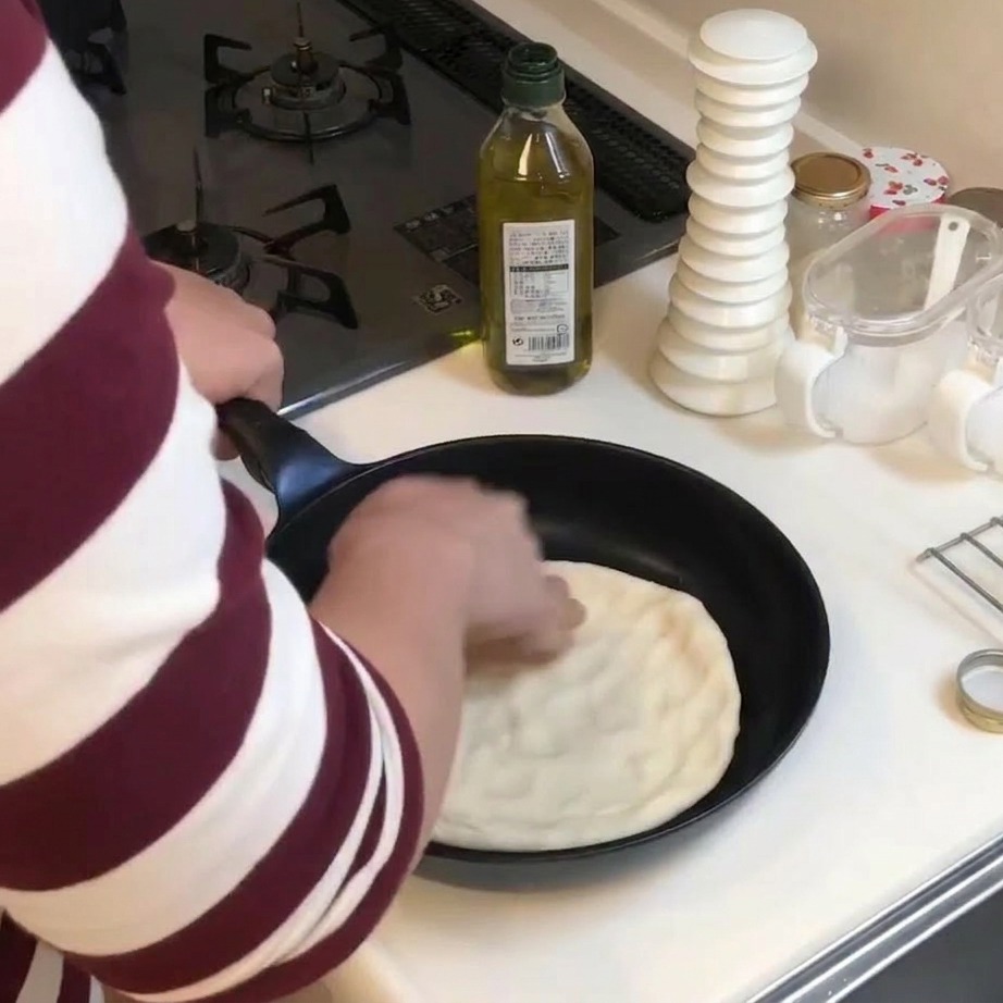 Une personne étalant de la pâte à pizza avec les doigts pour tapisser le fond dune poêle.