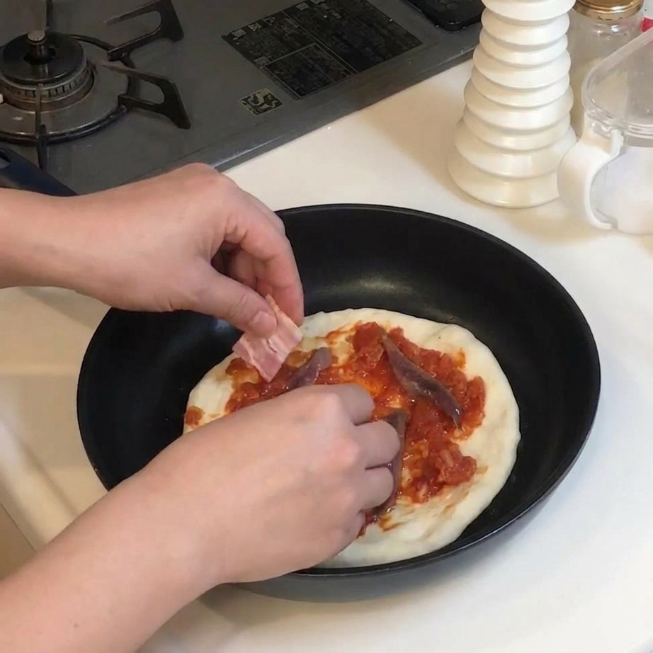 Des morceaux de lard cru déposés sur une pizza déjà garnie de sauce tomate et danchois.