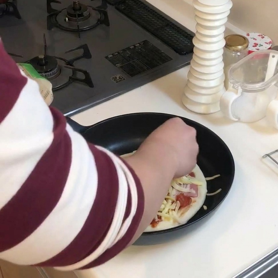 Une main parsemant généreusement de fromage râpé une pizza garnie dans une poêle.
