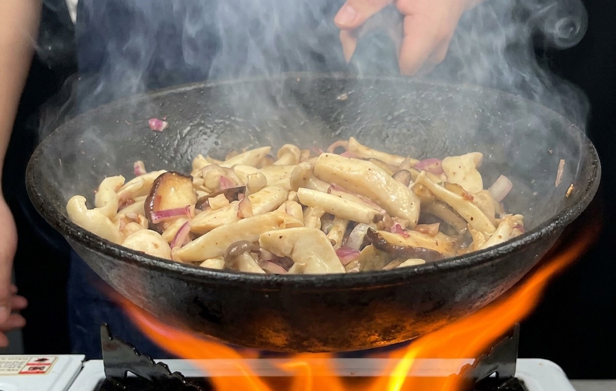 Une poêle remplie de champignons remuée vigoureusement au-dessus dune flamme de gaz vive avec de la vapeur sen échappant.