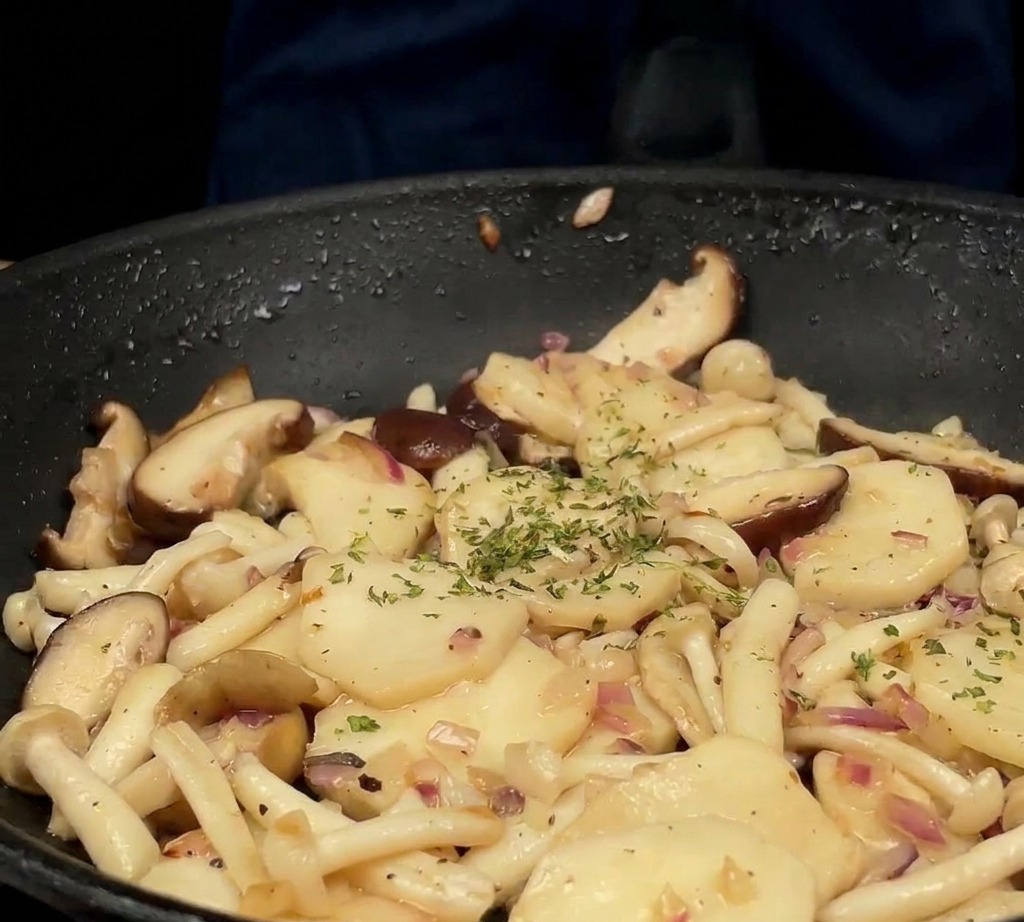 Persil vert frais haché saupoudré sur le mélange de champignons et doignons sautés dans une poêle noire.