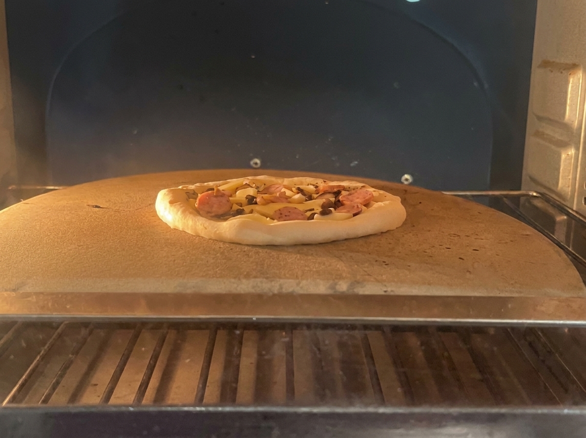 Une pizza non cuite garnie de pepperoni et de champignons sur une pierre de cuisson à lintérieur dun four professionnel.