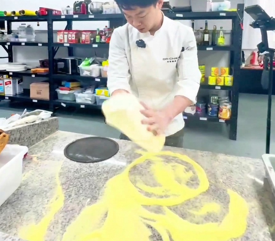Un chef étirant verticalement une base de pizza dans une cuisine professionnelle.