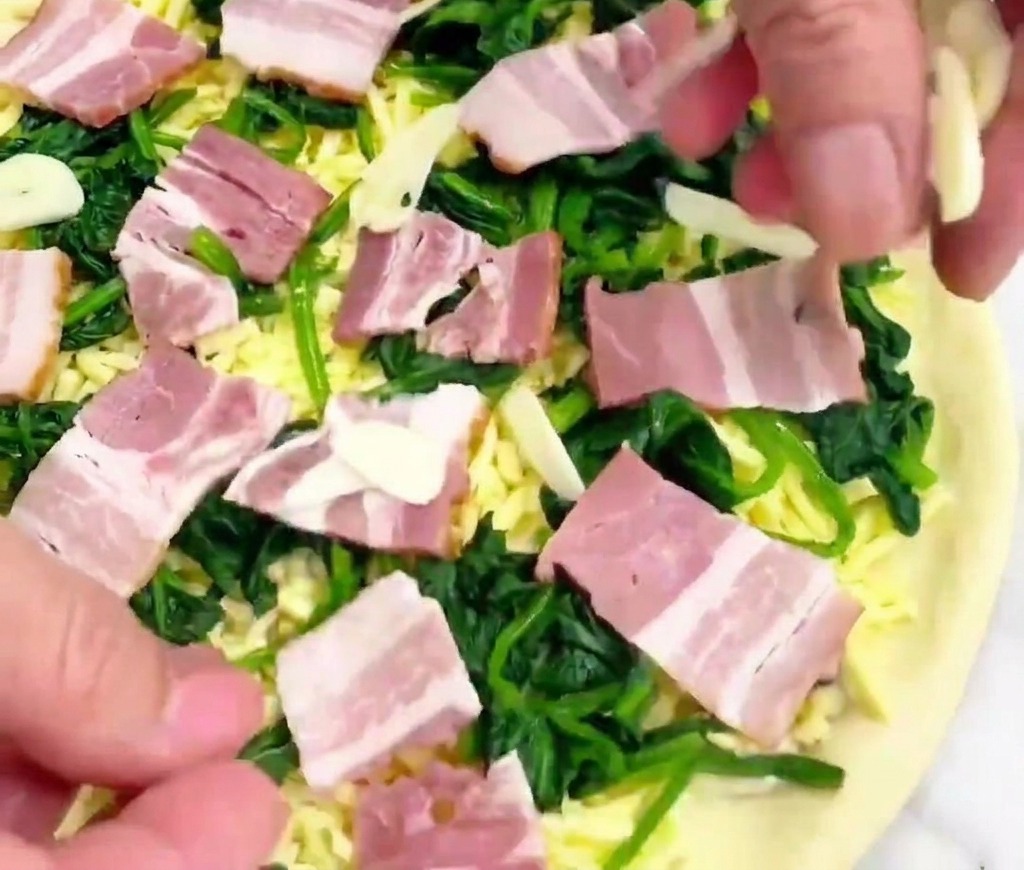 Une main déposant de fines lamelles dail sur une pizza prête à être enfournée.