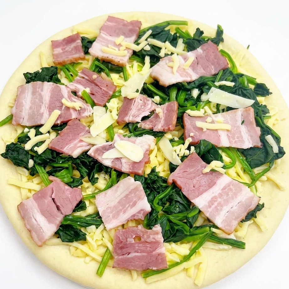 Vue aérienne dune pizza assemblée avec épinards, bacon et ail, surmontée dun léger voile de mozzarella.