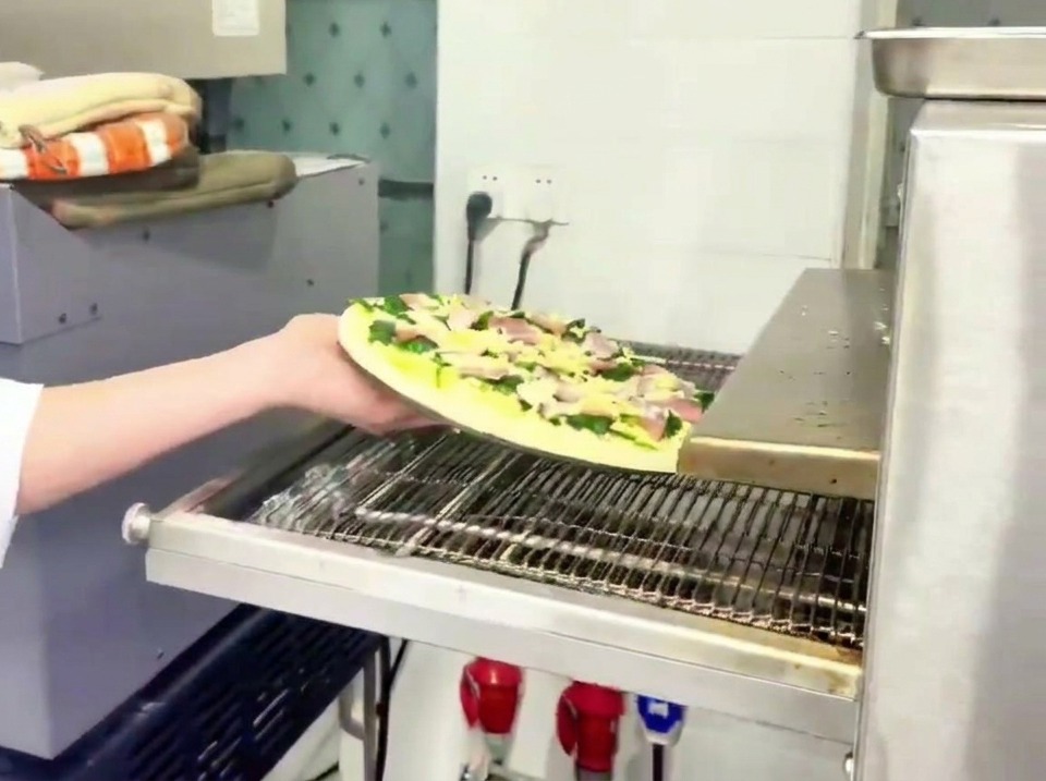 Un employé plaçant la pizza crue sur le tapis métallique dun four à pizza professionnel.
