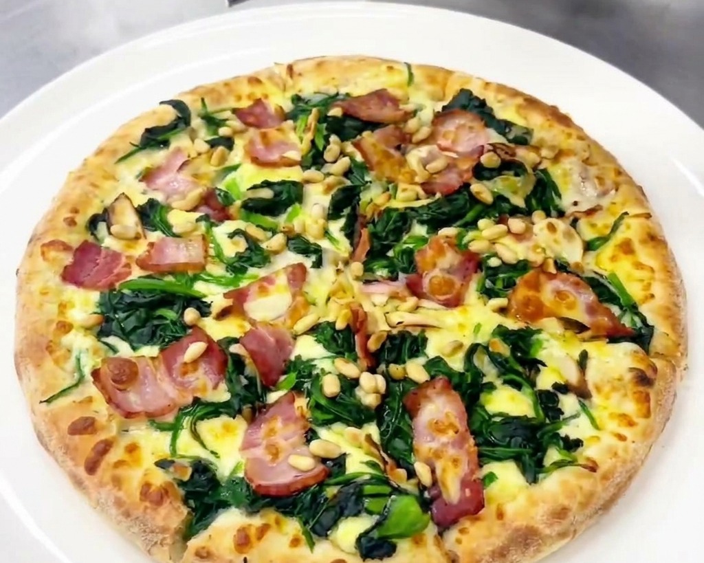 Une personne utilisant une râpe pour ajouter du parmesan frais sur une pizza cuite garnie dépinards et de bacon.