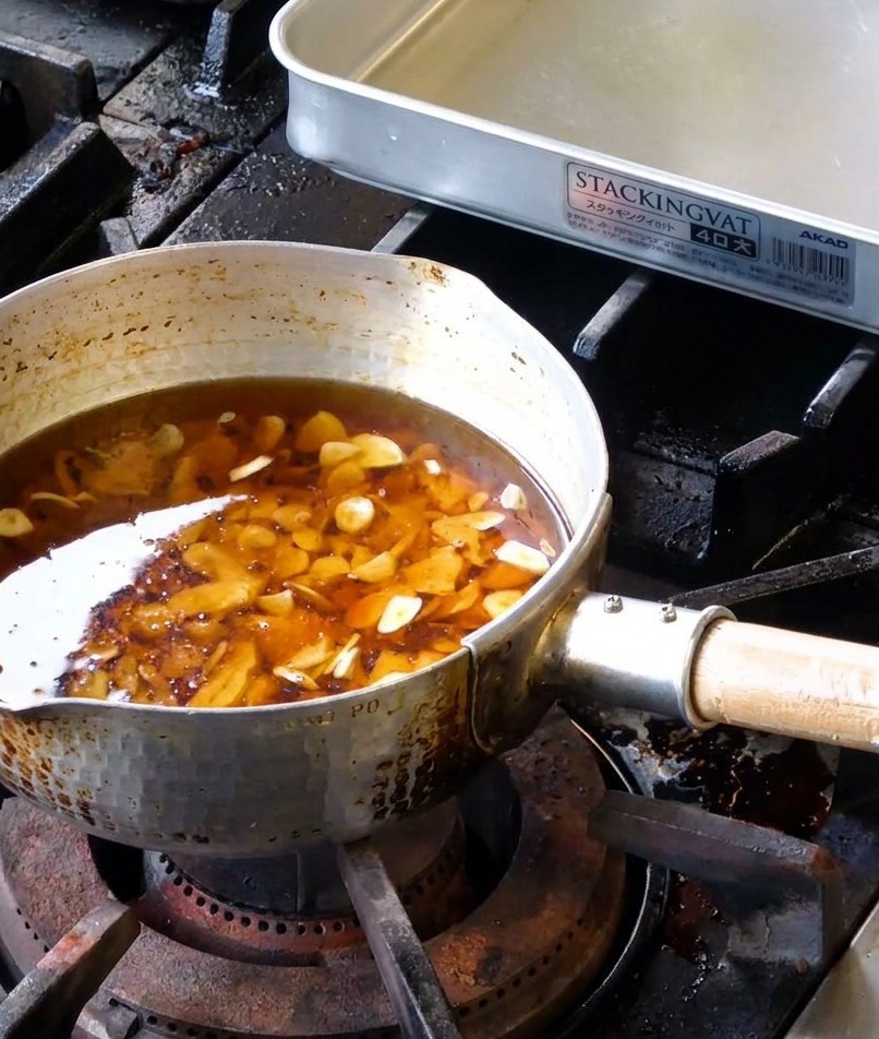 Différentes tranches dail cru immergées dans un mélange de saindoux liquide et dhuile de sésame dans une casserole en métal martelé.