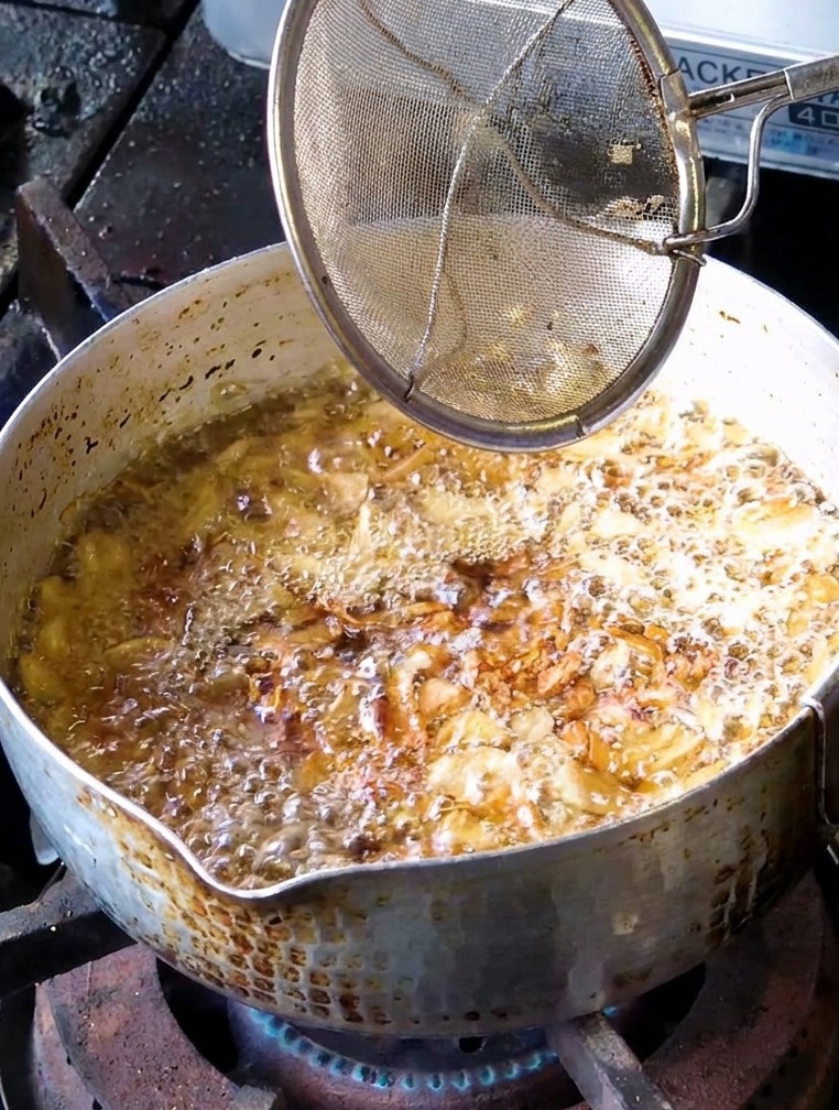 Une passoire fine utilisée pour récupérer des tranches dail frites dun brun doré clair dans une casserole dhuile bouillonnante.
