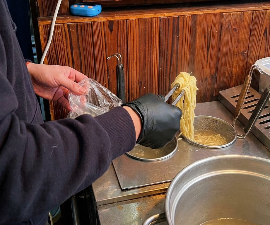 Une personne utilisant des pinces pour sortir des nouilles ramen dune casserole deau bouillante.