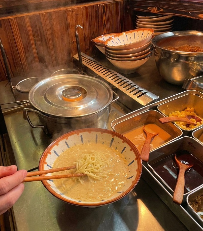 Utilisation de baguettes pour plier délicatement les nouilles ramen dans le bouillon crémeux.