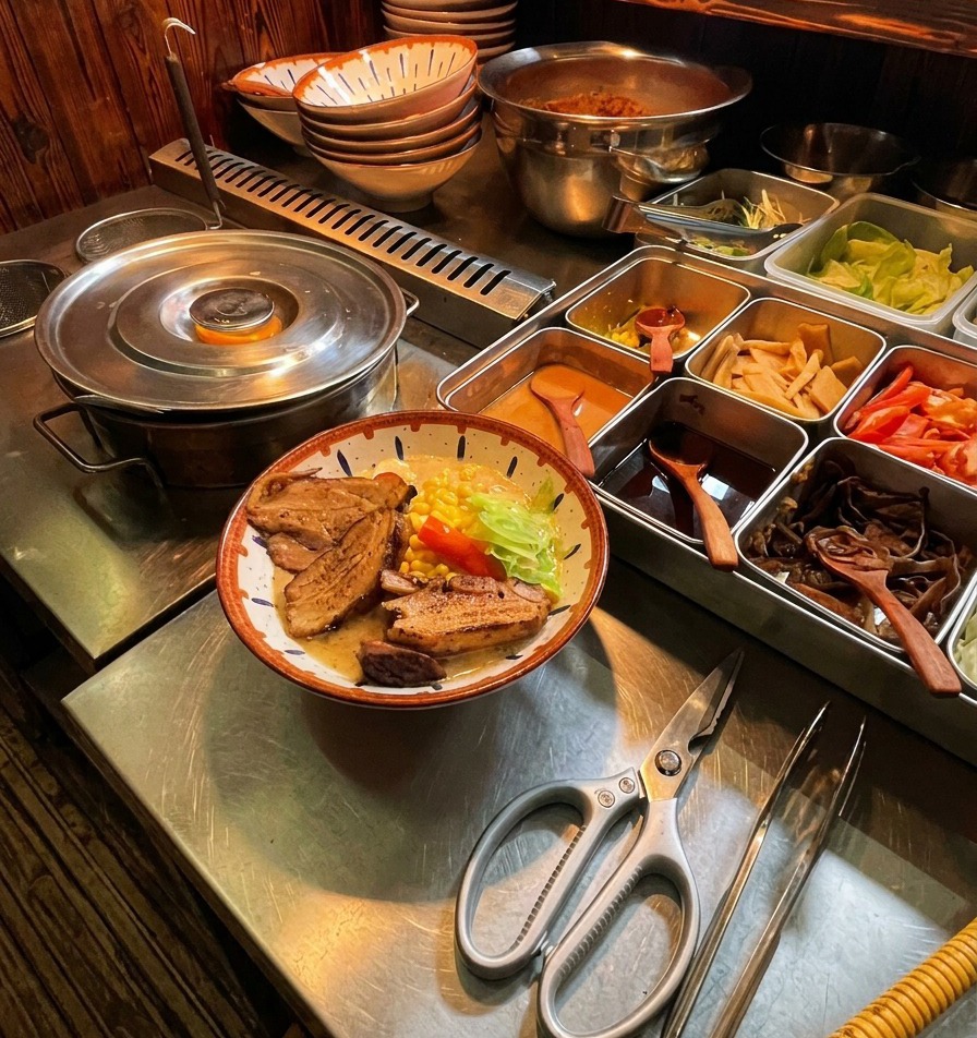 Tranches de porc chashu bien dorées déposées dans le bol de ramen à laide dune pince.
