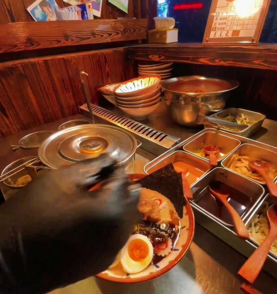 Une main versant de lhuile dail noire visqueuse sur les œufs mollets et la viande dans le ramen.