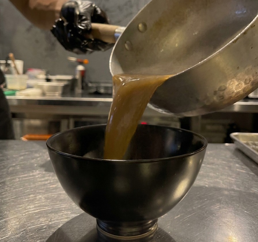 Bouillon brun à lail noir versé dans un petit bol de service noir.