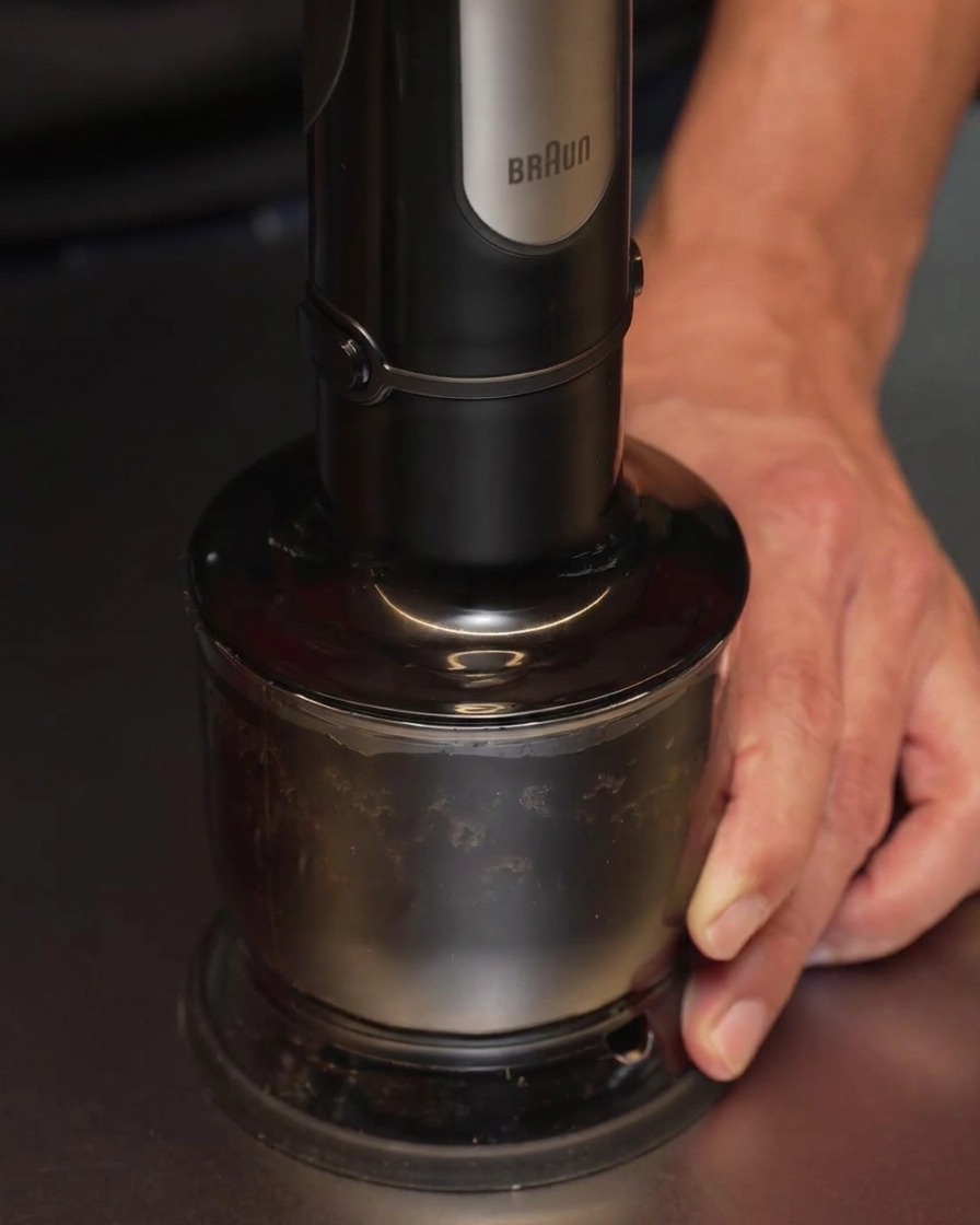Un mixeur plongeant utilisé pour transformer lail noirci et lhuile en un liquide noir lisse et opaque.